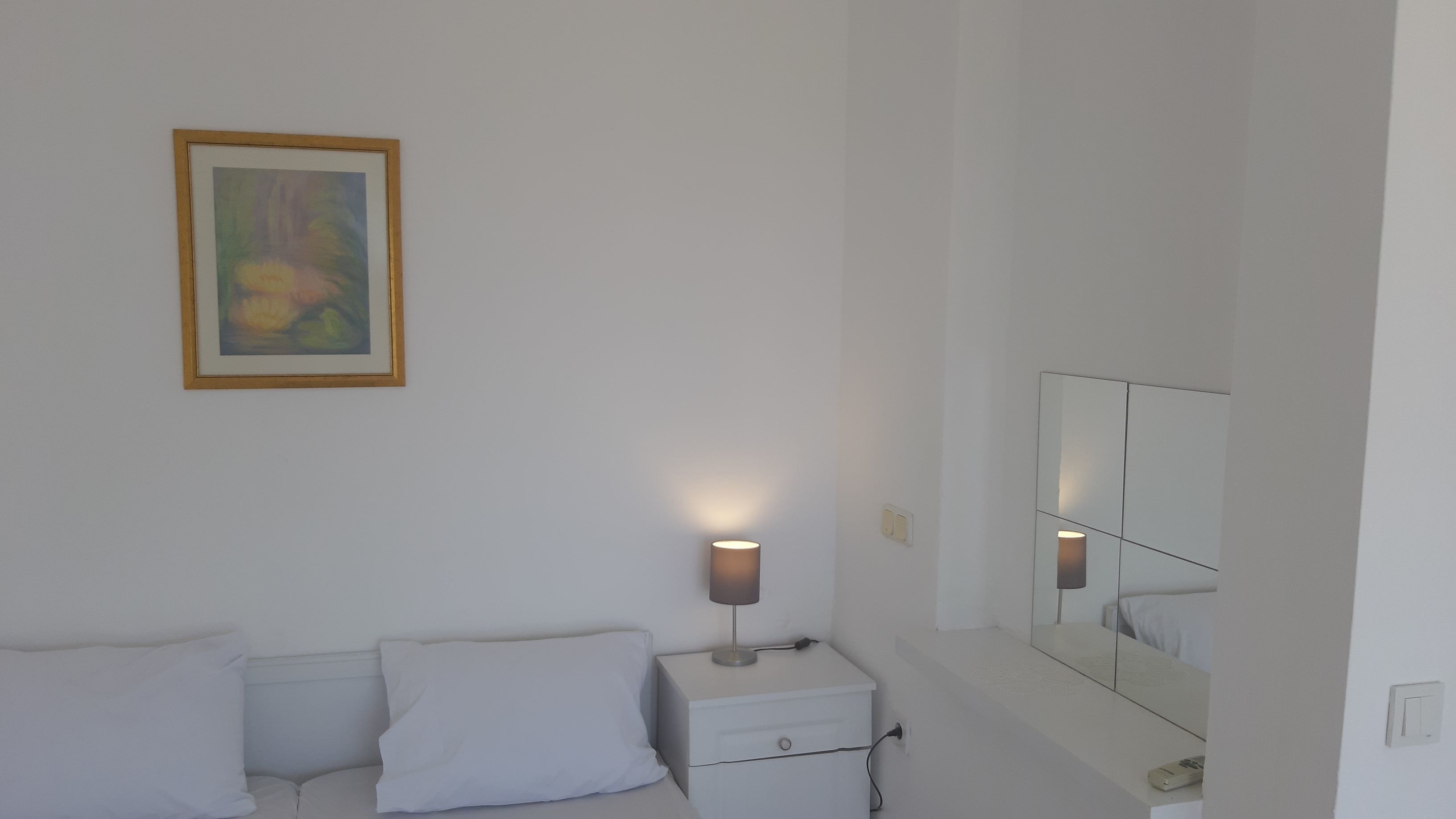 Un dormitorio minimalista con cama, mesita de noche, lámpara y un espejo grande.