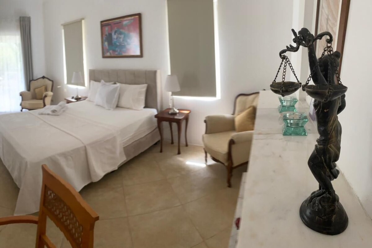 A hotel room with a large bed, two bedside tables, a chair, and a decorative sculpture.