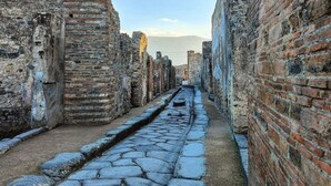 Una estrecha calle adoquinada bordeada por antiguas paredes de ladrillo, que conduce a una vista distante de montañas.