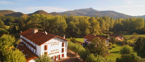 A white building with a red roof, surrounded by trees and hills.