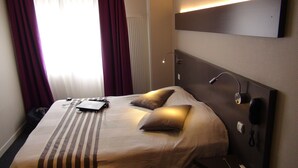 Quarto de hotel com uma cama, mesa de cabeceira, abajur e telefone.