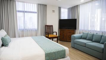Une chambre d’hôtel avec un lit, un canapé, une télévision et des rideaux.