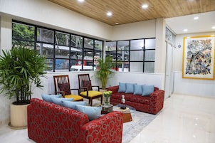 Un salón espacioso con un sofá rojo, cojines azules, una mesa de centro de madera y ventanas grandes que ofrecen vistas al exterior.