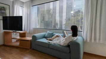 Una sala de estar moderna con un sofá, un televisor de pantalla plana y un ventanal con cortinas.
