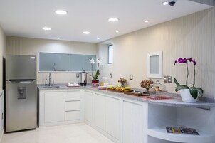Una cucina moderna con mobili bianchi, un frigorifero in acciaio inossidabile e un piano di lavoro con frutta e fiori.
