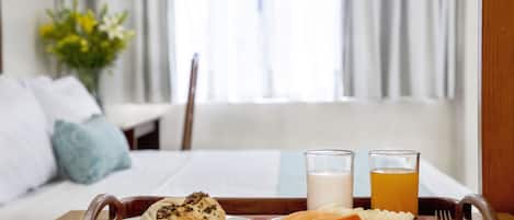 Un plateau de petit-déjeuner avec des viennoiseries, des fruits, et deux verres de lait et de jus, posé sur un plateau en bois dans une chambre d’hôtel.