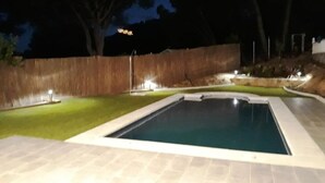 Una piscina con solárium empedrado, rodeada por una cerca de madera y un césped.