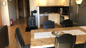 A modern kitchen with white cabinets, a stainless steel refrigerator, a built-in oven, and a wood-burning stove. - Randsverk Hytter i Lemonsjøen Fjellpark (Vaga)