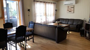 A cozy living area with a wooden dining table, chairs, a sofa, and a window with curtains. - Randsverk Hytter i Lemonsjøen Fjellpark (Vaga)