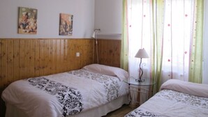 Un dormitorio con dos camas, paneles de madera en las paredes, una mesita de noche pequeña con una lámpara y dos cuadros colgados.