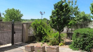 Un espacio exterior amurallado con un sendero pavimentado, jardineras de madera y una farola.