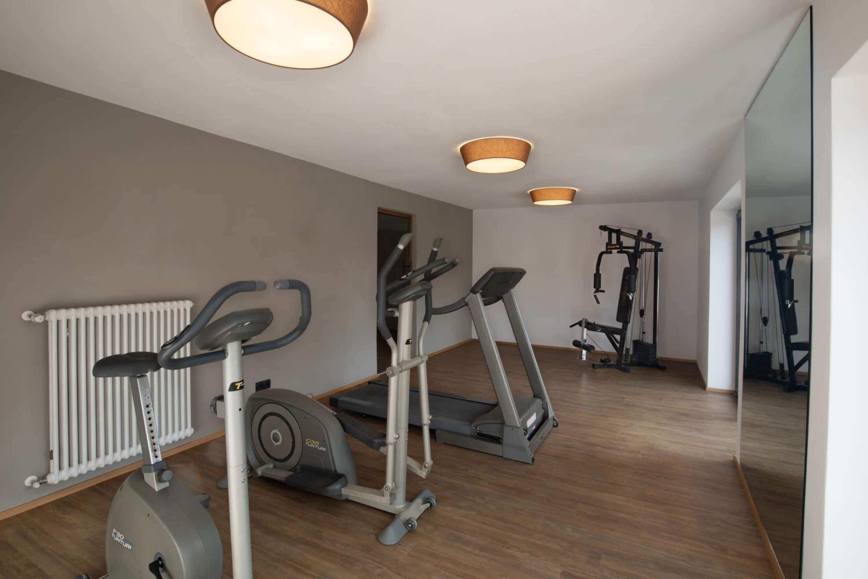 A modern gym with cardio machines, a mirrored wall, and a radiator.