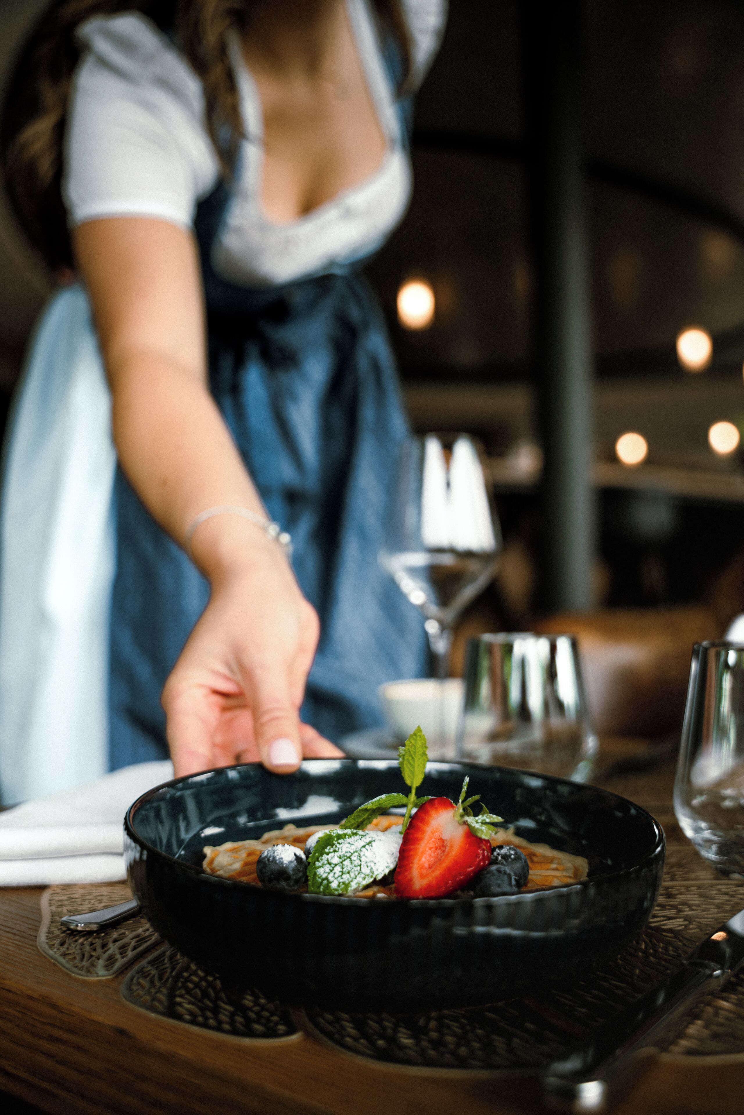 Une personne présente un plat dans un bol noir, sur une table recouverte d’un set de table.
