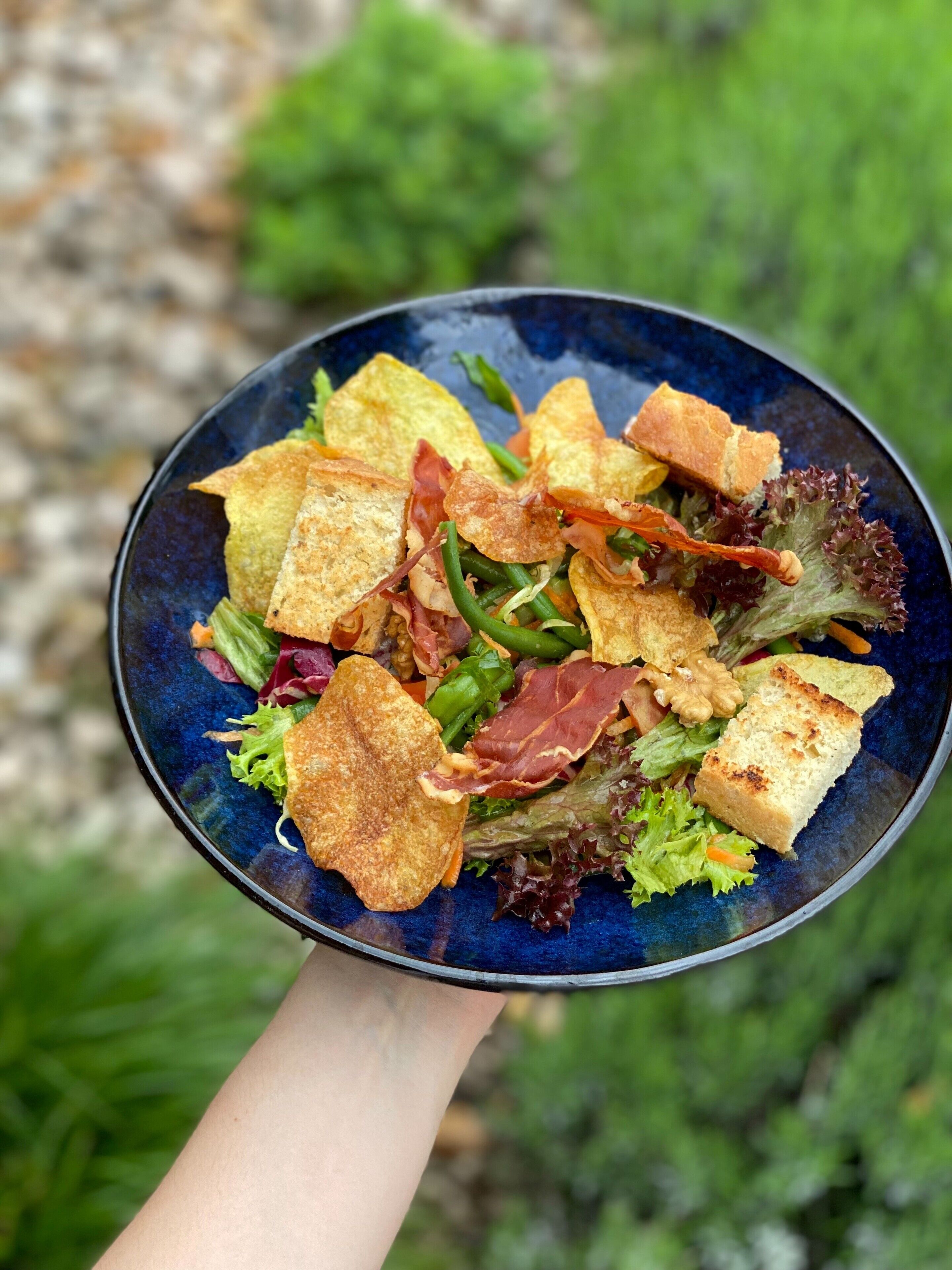 A bowl of salad with various ingredients, held by a person.