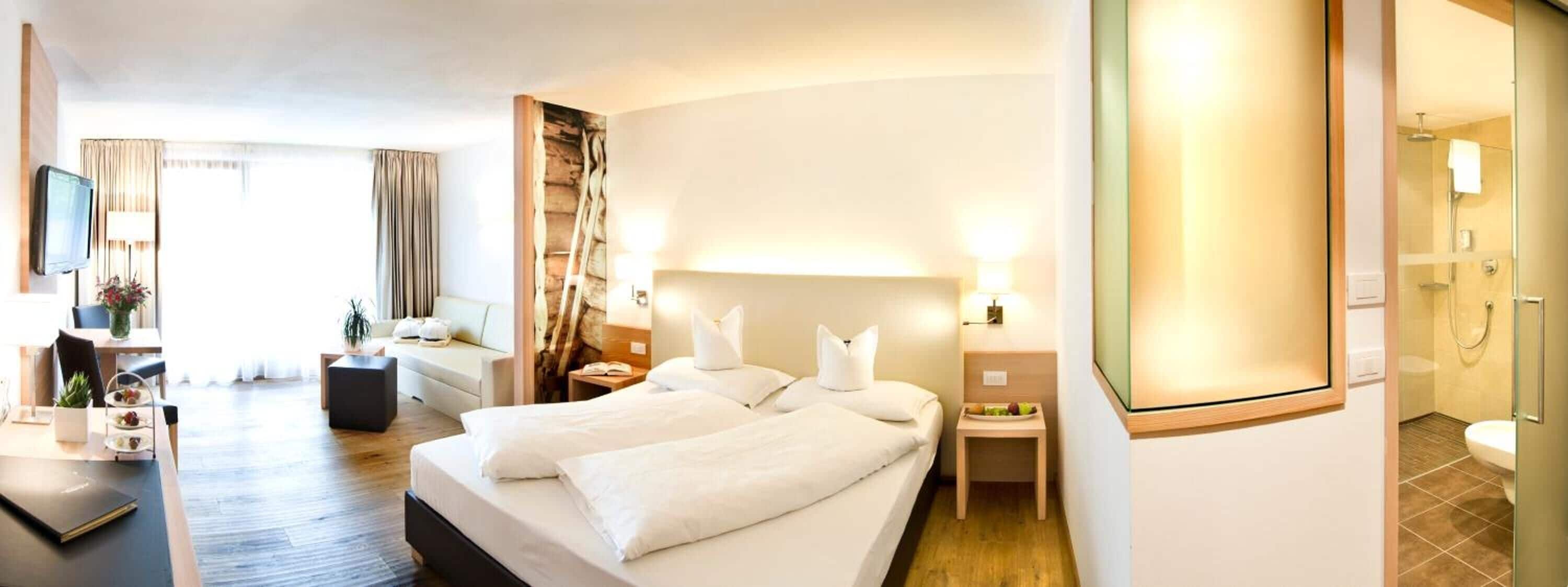 Ein Hotelzimmer mit einem großen Bett, Nachttischen, einem Fernseher, einem Schreibtisch mit Stuhl und einem kleinen Tisch mit Früchten.