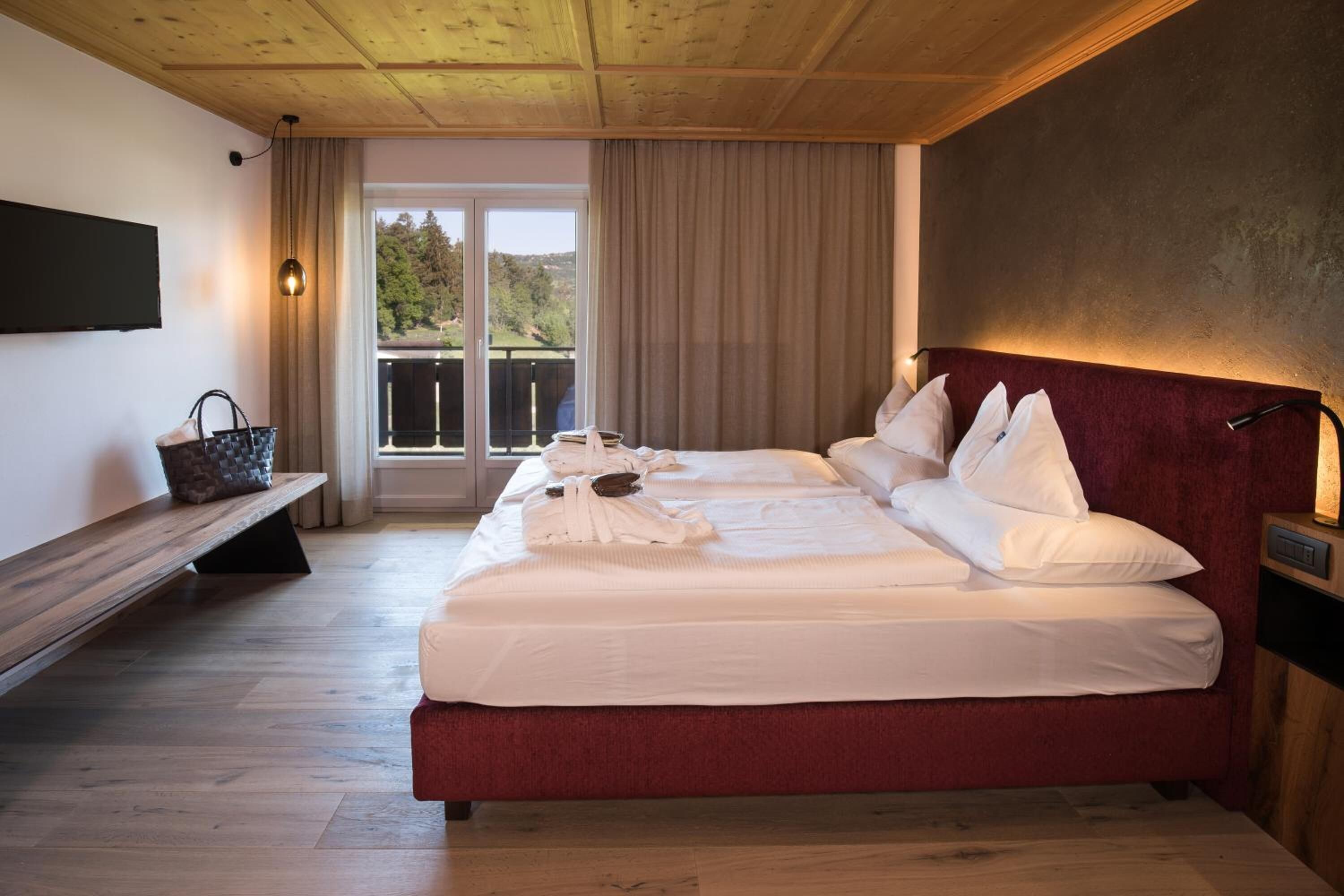 A hotel room with a large bed, a bench, a TV, and a view of the outdoors.