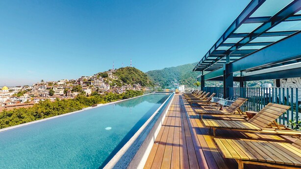 A rooftop pool with wooden loungers and a view of a hillside town. - Legendary Mexican Architecture in the Heart of Zona Romantica! 1BD Studio for re (Puerto Vallarta)