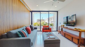 A modern living room with a sofa, ottoman, and a red armchair. A flat-screen TV is mounted on the wall, and there is a wooden console table with a tray. - Legendary Mexican Architecture in the Heart of Zona Romantica! 1BD Studio for re (Puerto Vallarta)