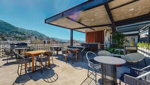 An outdoor terrace with tables and chairs, a barbecue grill, and a view of the city and hills. - Legendary Mexican Architecture in the Heart of Zona Romantica! 1BD Studio for re (Puerto Vallarta)