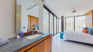 A modern bedroom with a large bed, a bathroom with a vanity, and a city view through large windows. - Legendary Mexican Architecture in the Heart of Zona Romantica! 1BD Studio for re (Puerto Vallarta)