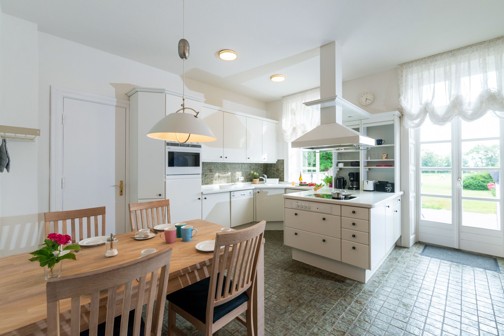 A modern kitchen with white cabinets, a wooden dining table, and pendant lights.