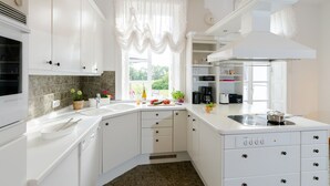 Una cocina moderna con armarios blancos, horno integrado y una ventana con cortinas ligeras.