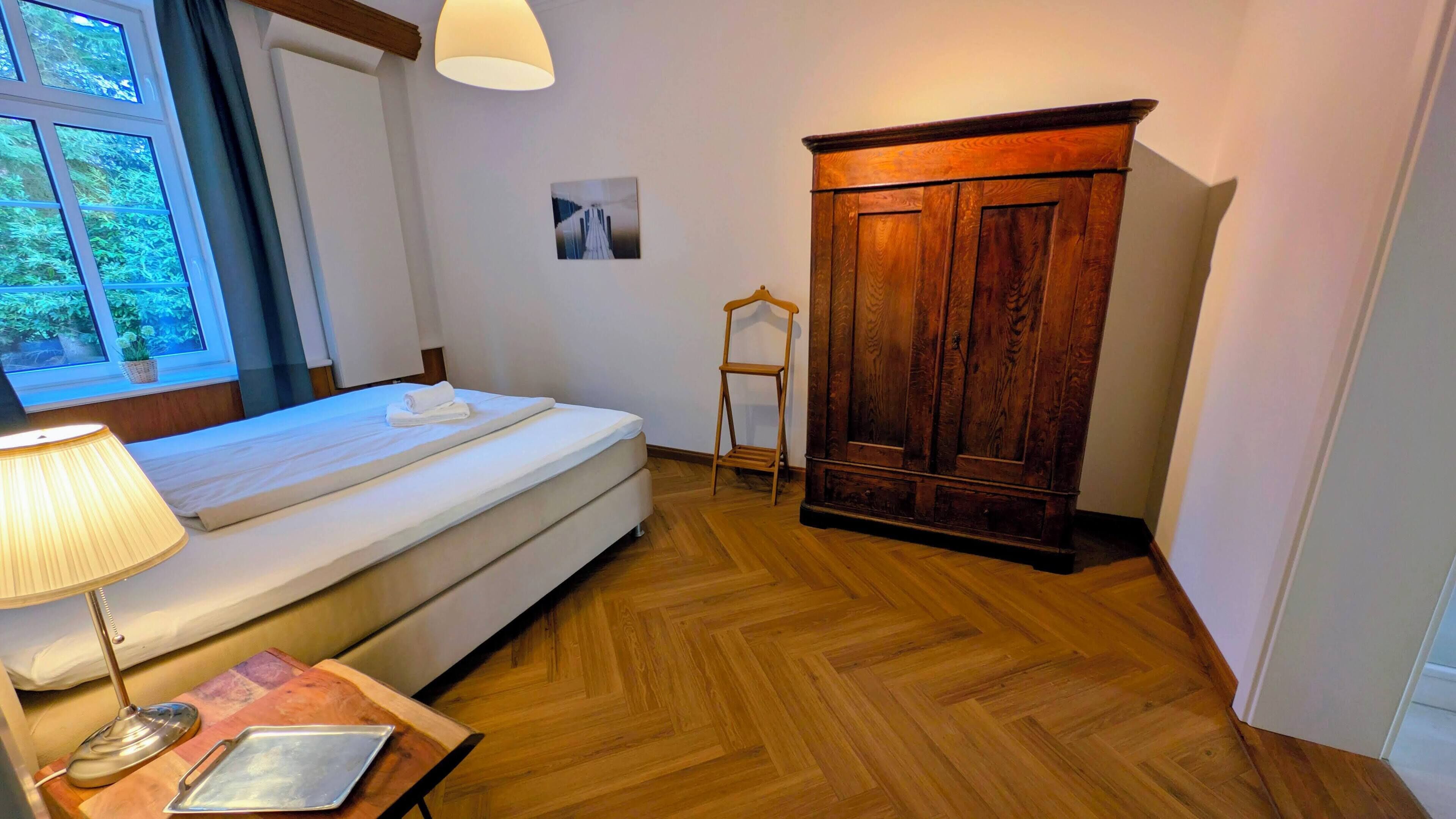 Une chambre à coucher comprenant un lit, une armoire en bois, une table de chevet avec une lampe et une fenêtre donnant sur un paysage verdoyant.