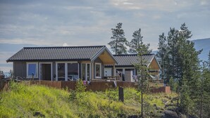 A two-story cabin with a sloped roof, large windows, and a wooden deck.