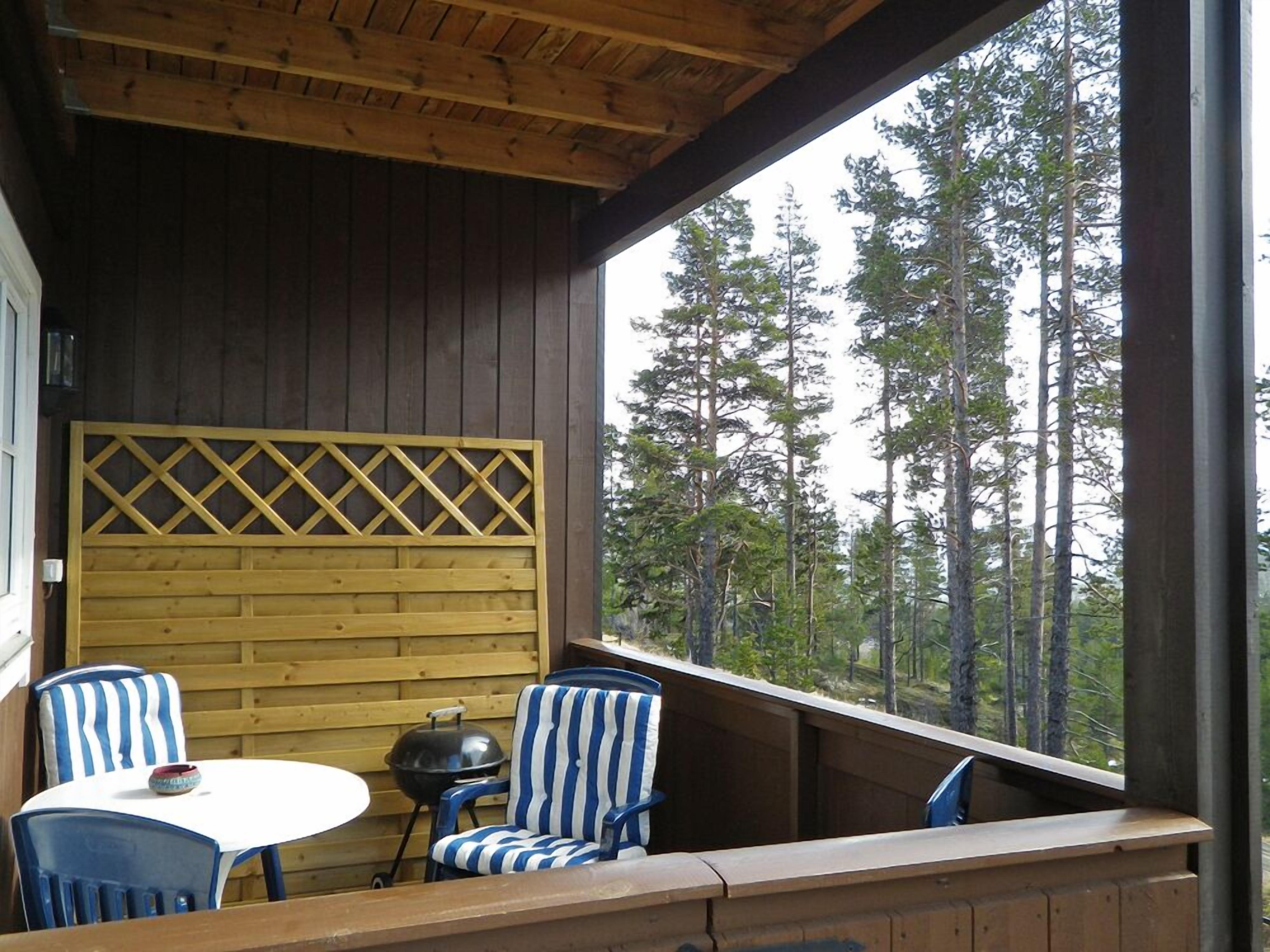 A wooden deck with two blue-striped chairs and a small table, overlooking a forest.
