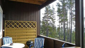 A wooden deck with two blue-striped chairs and a small table, overlooking a forest.