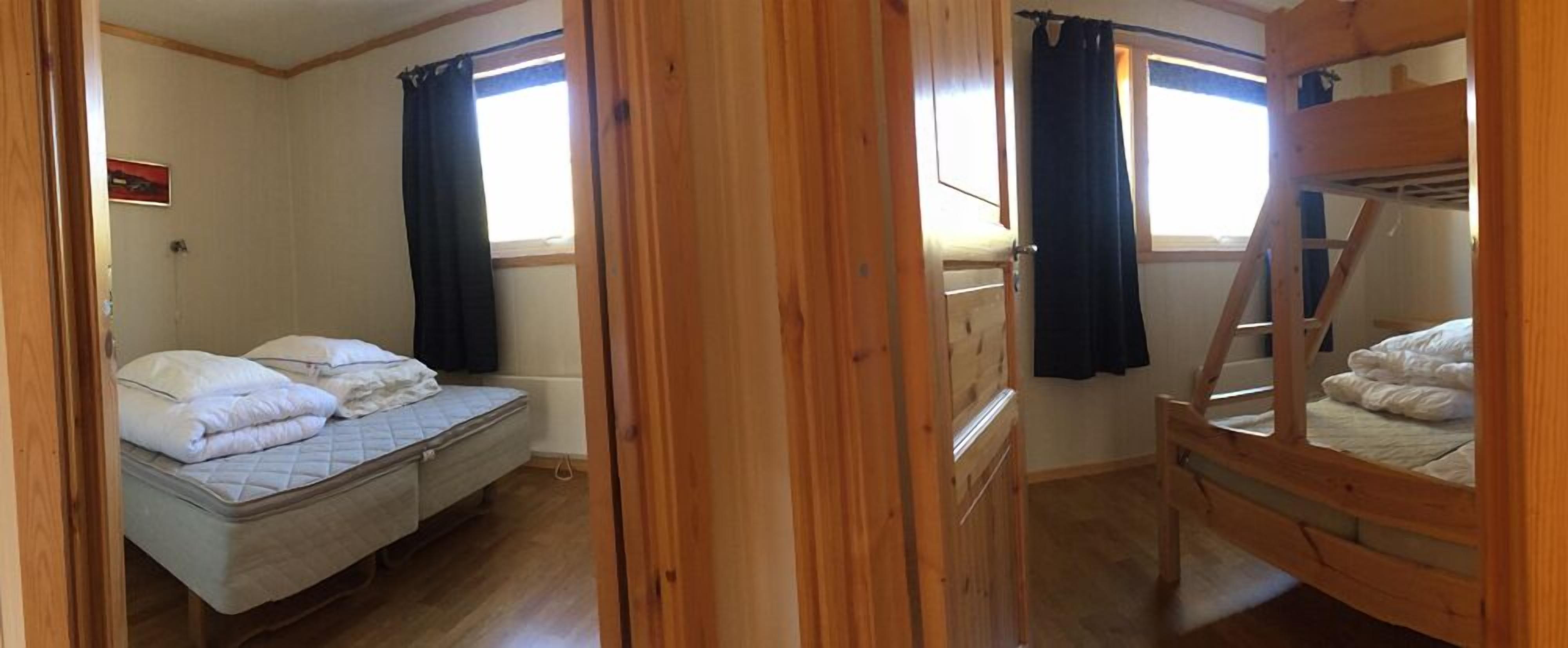 Een slaapkamer met een stapelbed en een eenpersoonsbed, houten vloeren en een raam met gordijnen.