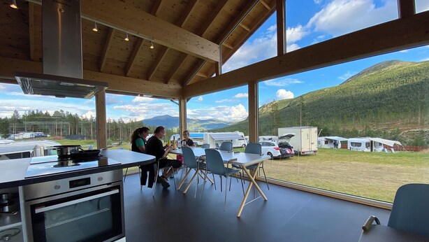 A modern kitchen with large windows, a dining area, and a view of a campsite.