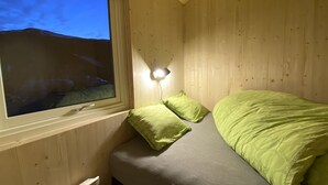 A small, cozy room with a bed, a window, and a wall-mounted light.