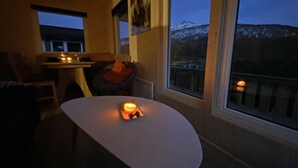 A cozy room with a dining table and chairs, a small table with a candle, and large windows offering a view of snow-capped mountains.