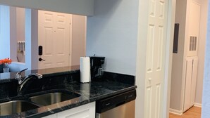 A modern kitchen with white cabinets, a stainless steel dishwasher, and a black granite countertop.