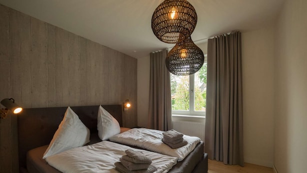 Un dormitorio moderno con una cama grande, dos lámparas de noche, una lámpara colgante de tejido y vistas a zonas verdes a través de la ventana.