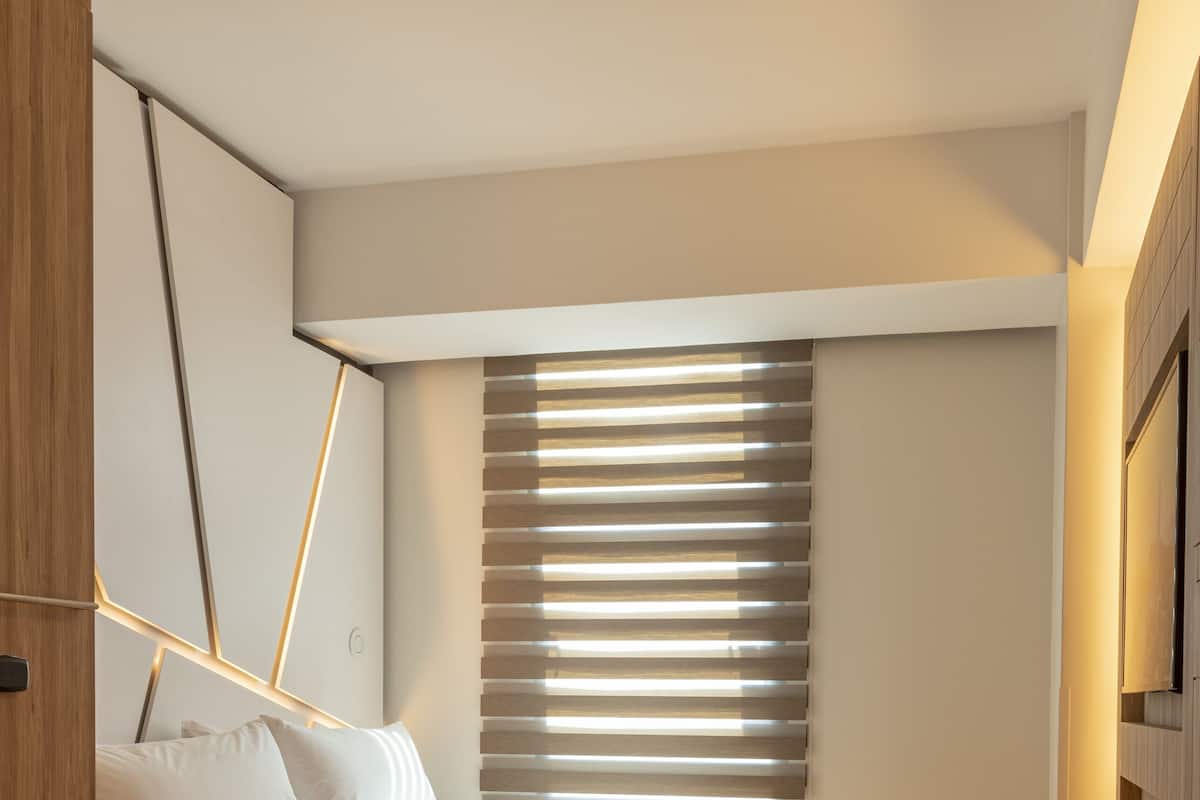 Un dormitorio moderno con cama, suelo de madera, techo inclinado y un amplio ventanal con persianas.