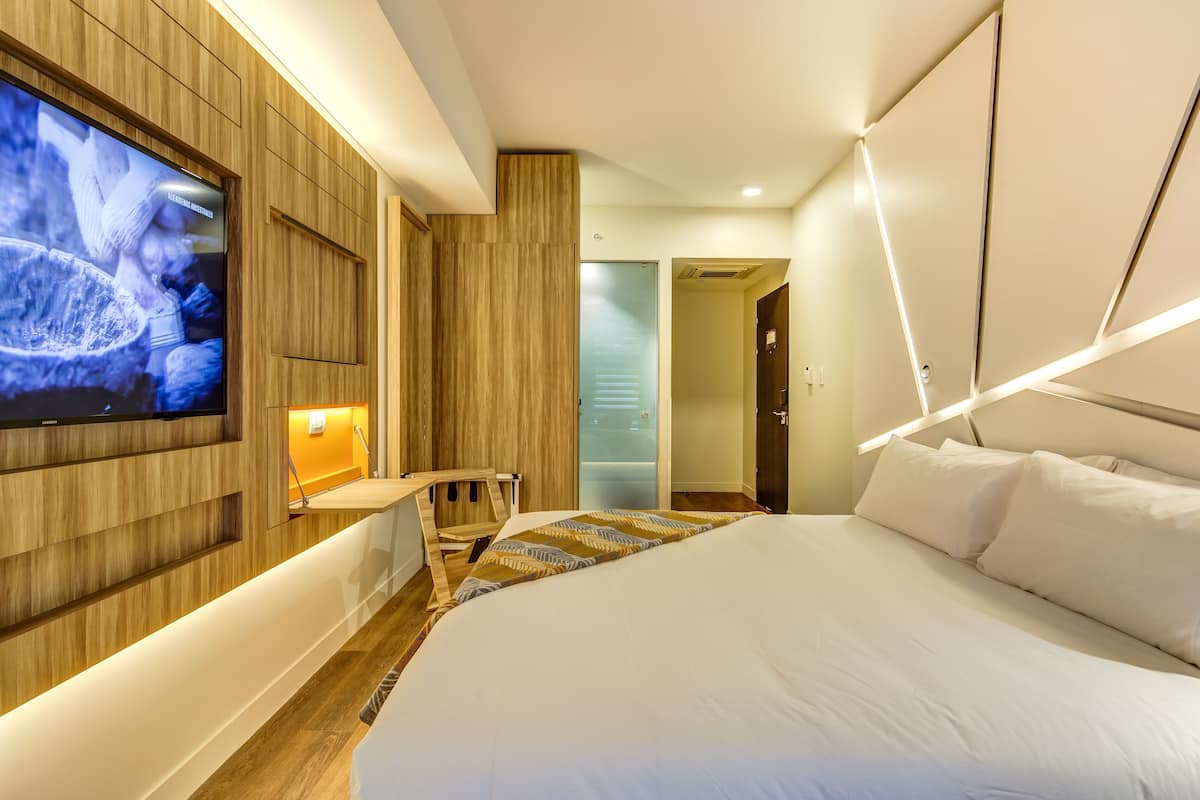 Una habitación de hotel moderna con una cama grande, un televisor de pantalla plana en la pared y una pared decorativa de madera, además de una pequeña zona de estar.