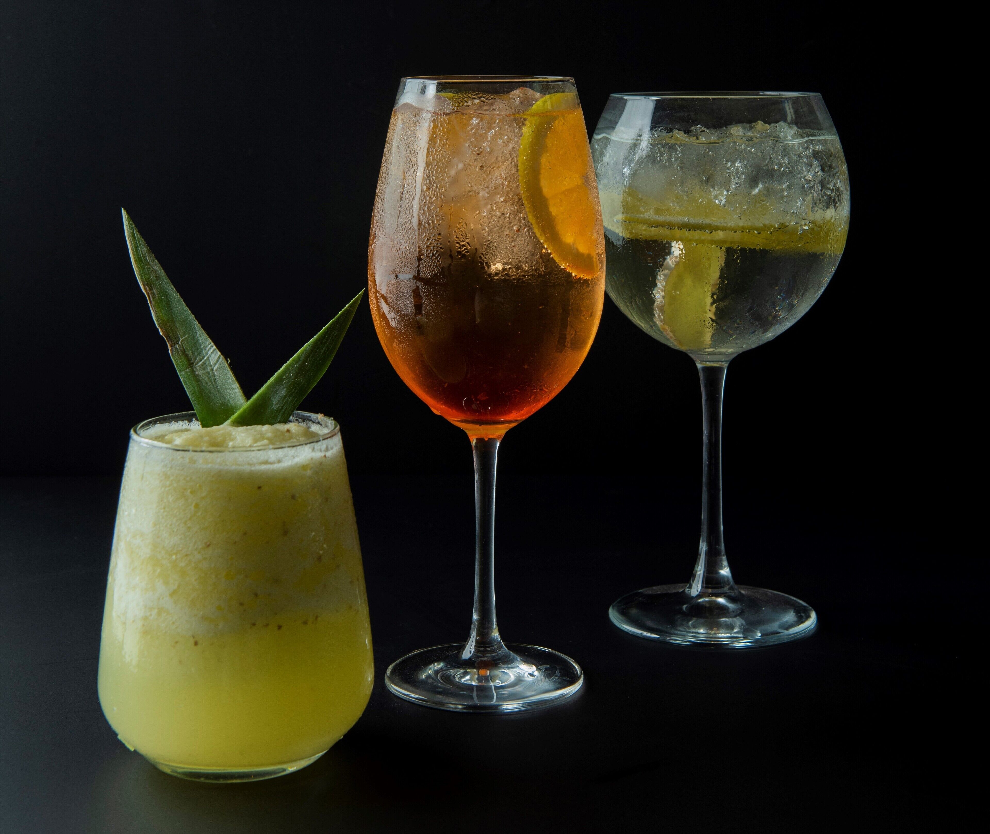Three glasses of beverages with different garnishes against a dark background.