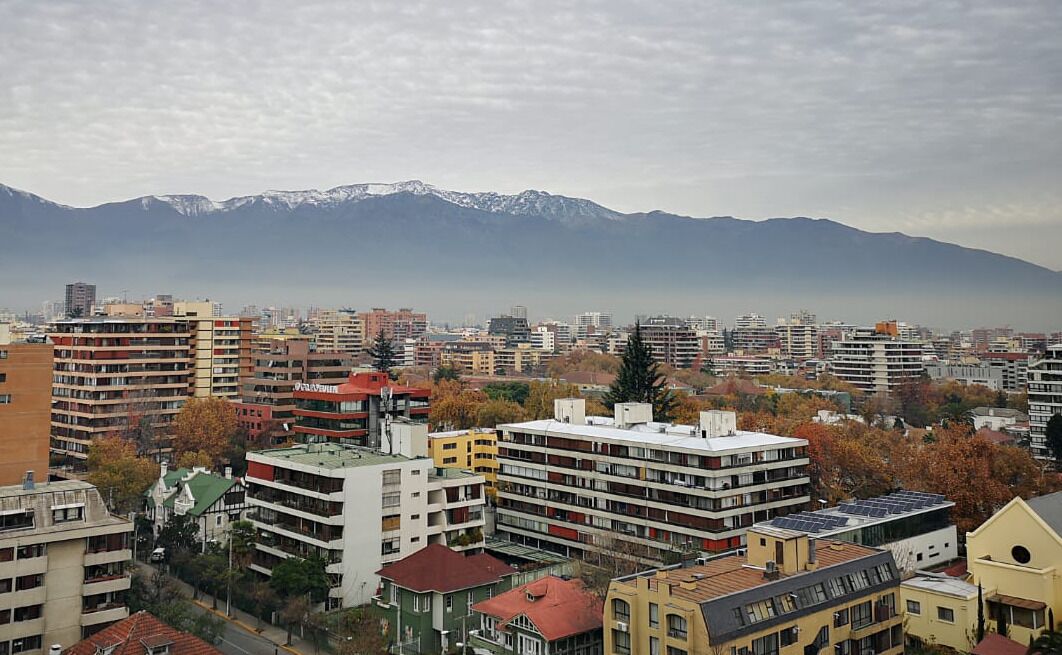 Un paisaje urbano con edificios de varios pisos, una combinación de estructuras residenciales y comerciales, y una cadena montañosa al fondo.