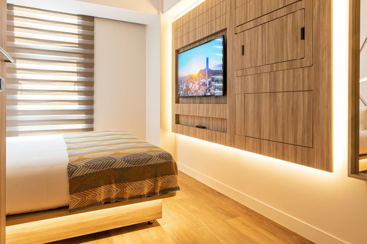 Un dormitorio moderno con cama, panel de madera, televisor y persianas.