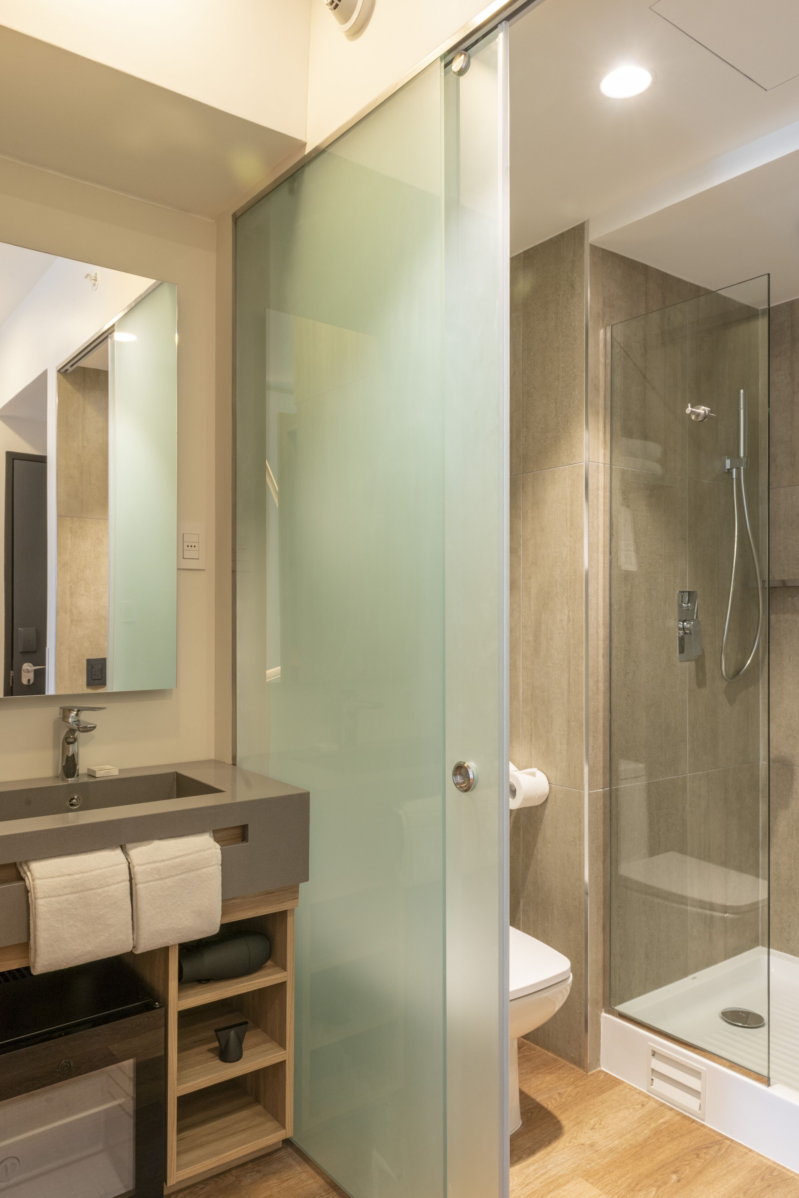 Un baño moderno con cabina de ducha de vidrio, un lavabo con toallero y un inodoro.