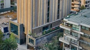 A modern high-rise building with a unique vertical design, surrounded by other buildings and construction cranes in the background. - Hotel Nodo - El primer hotel de negocios en Chile (Santiago)