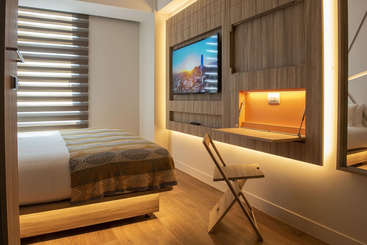 Una habitación de hotel moderna con una cama, un televisor montado en la pared y un escritorio con una silla.