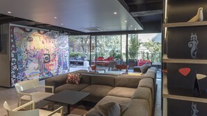 A modern lounge area with a large abstract mural, comfortable seating, and a view of the outdoors. - Hotel Nodo - El primer hotel de negocios en Chile (Santiago)