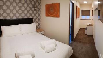 Ein Hotelzimmer mit Bett, Nachttisch, einer Wand mit Blattmuster und einem Gemälde.