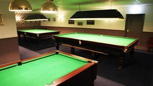 A pool table area with multiple tables, overhead lighting, and a door in the background. - The Kingstanding Inn (Birmingham)