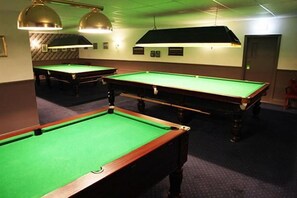 A pool table area with multiple tables, overhead lighting, and a door in the background. - The Kingstanding Inn (Birmingham)