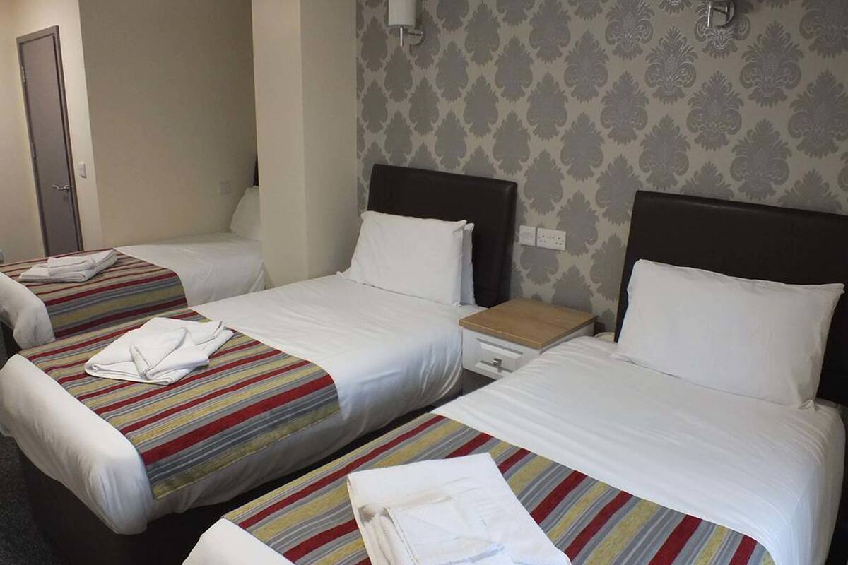 A hotel room with two single beds, each with a striped bedspread and a white pillow. There is a nightstand with a lamp between the beds.