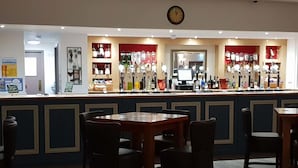 A bar area with a counter displaying various bottles and glasses, surrounded by wooden tables and chairs. - The Kingstanding Inn (Birmingham)